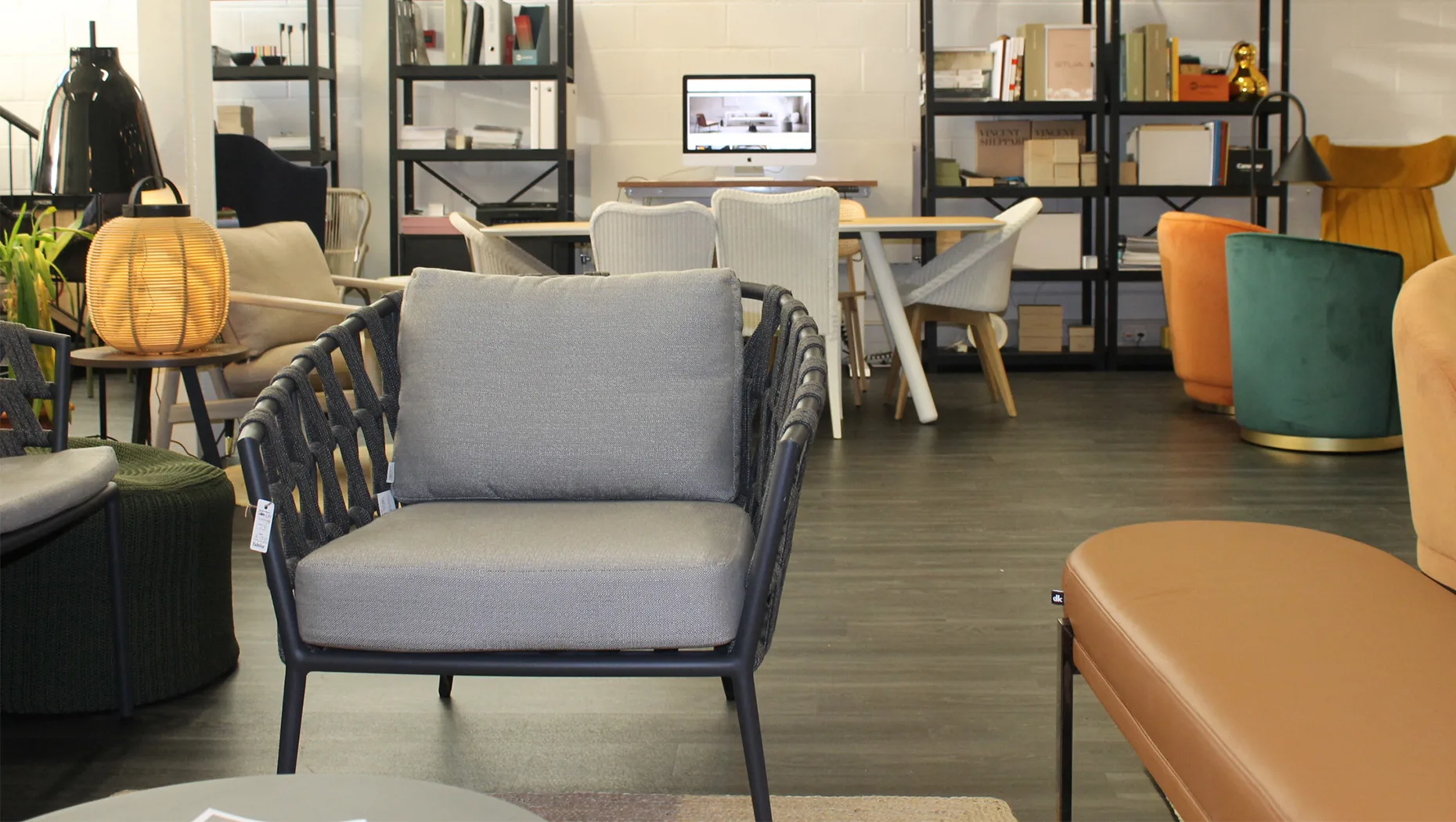 a shot of a comfortable lounge armchair with cushioned seats and backs, featuring lloyd loom and dining chairs in the background